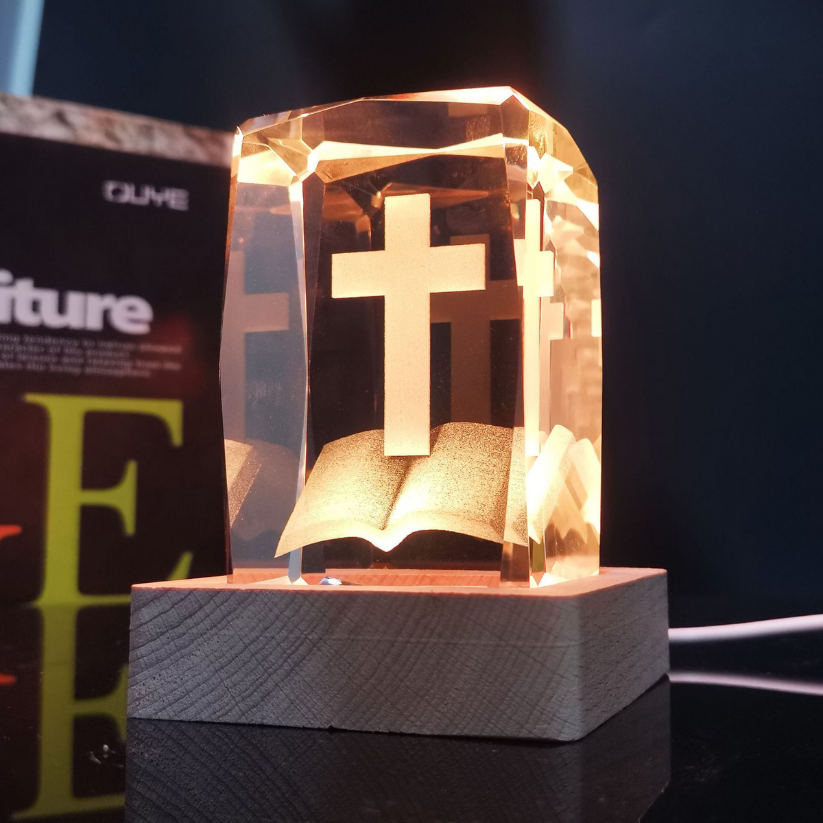 Cruz de cristal con Biblia abierta encendida con luz cálida sobre base de madera